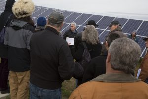 A tour group listens as Tim Holmes talks about the solar field while standing in front of a solar panel
