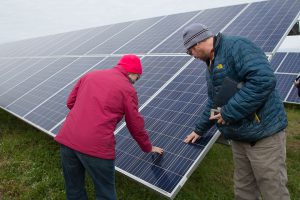 Two people in winter coats touch a solar panel