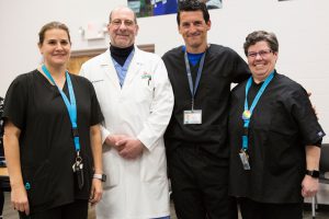 Four adults, three in black scrubs and one in a white doctor's coat, in a group portrait