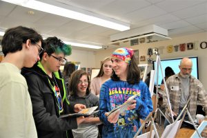 Students in a classroom look at and discuss artwork.