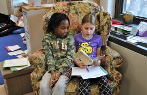 Two students sharing a book and a chair.
