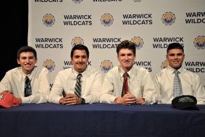 Four students sitting at draped table. A backdrop is imprinted with Wildcats and district logos