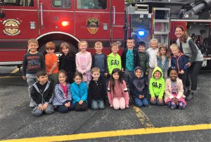 A class and their teacher pose in front of a fire engine.