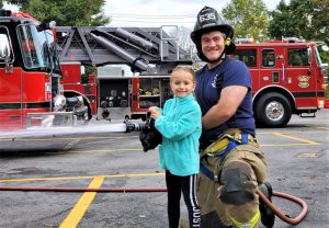 A firefighter helps a student holding a jetting fire hose