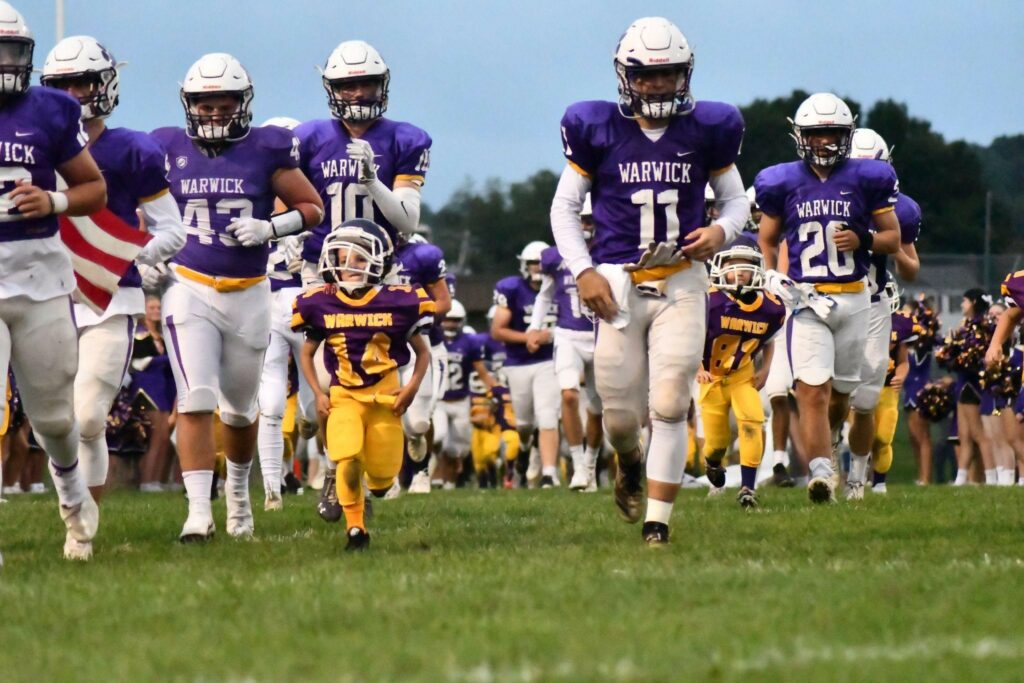 Warwick football players take the field with youth football players