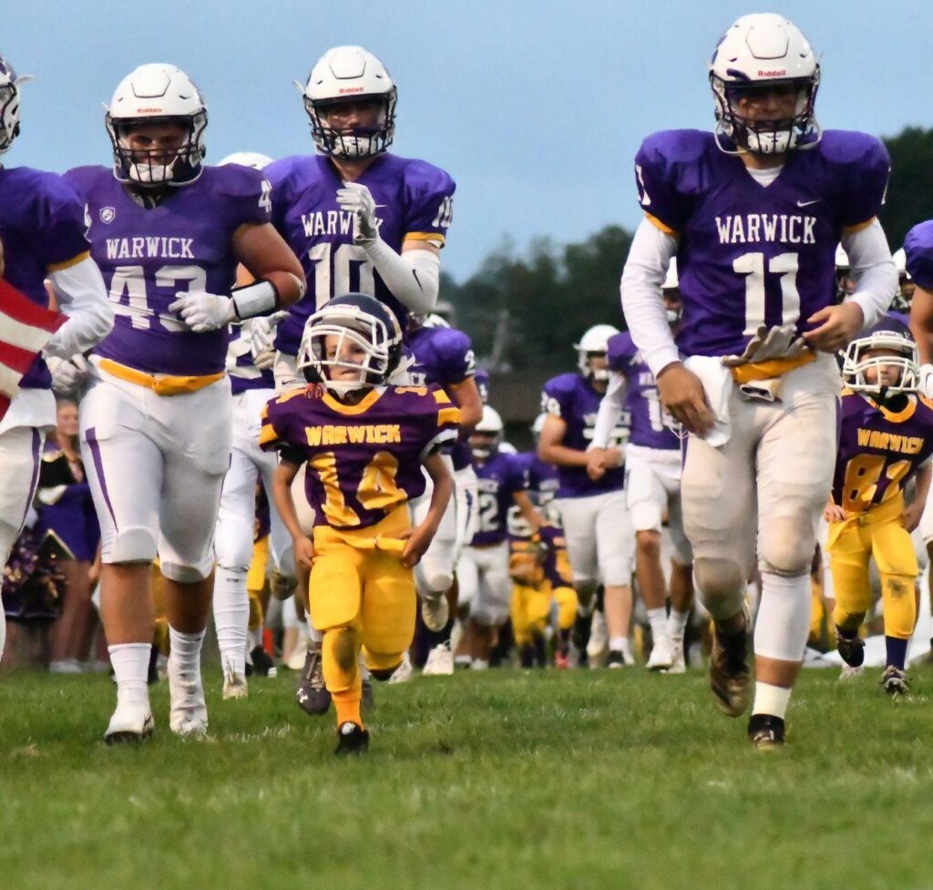 Warwick football players take the field with youth football players
