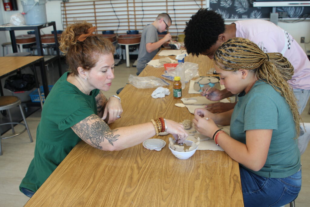 Ms. Sisco on the left and a student on the right working on the student's clay art
