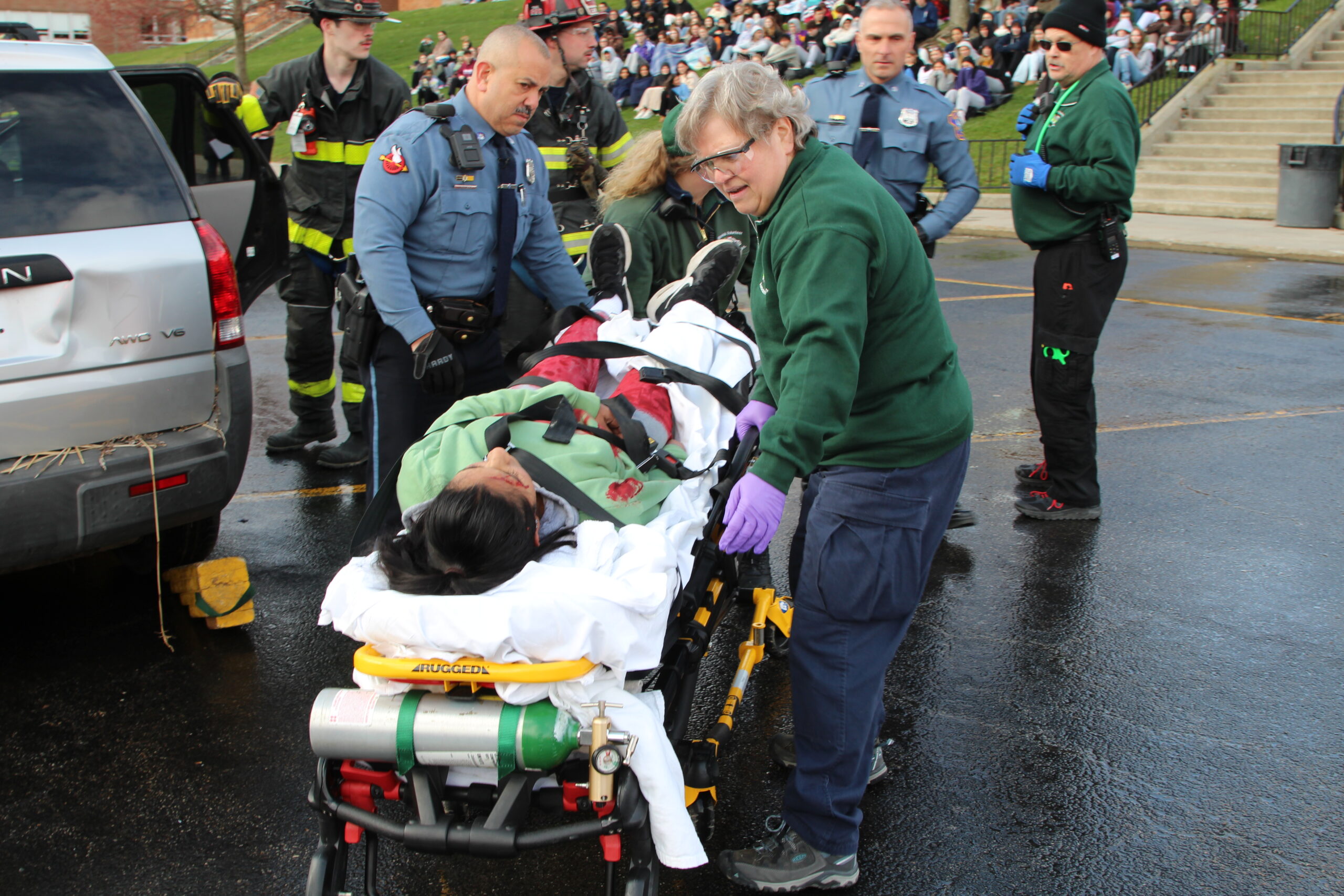 A student is transported to an ambulance in a mock crash event along with a police officer and an EMT