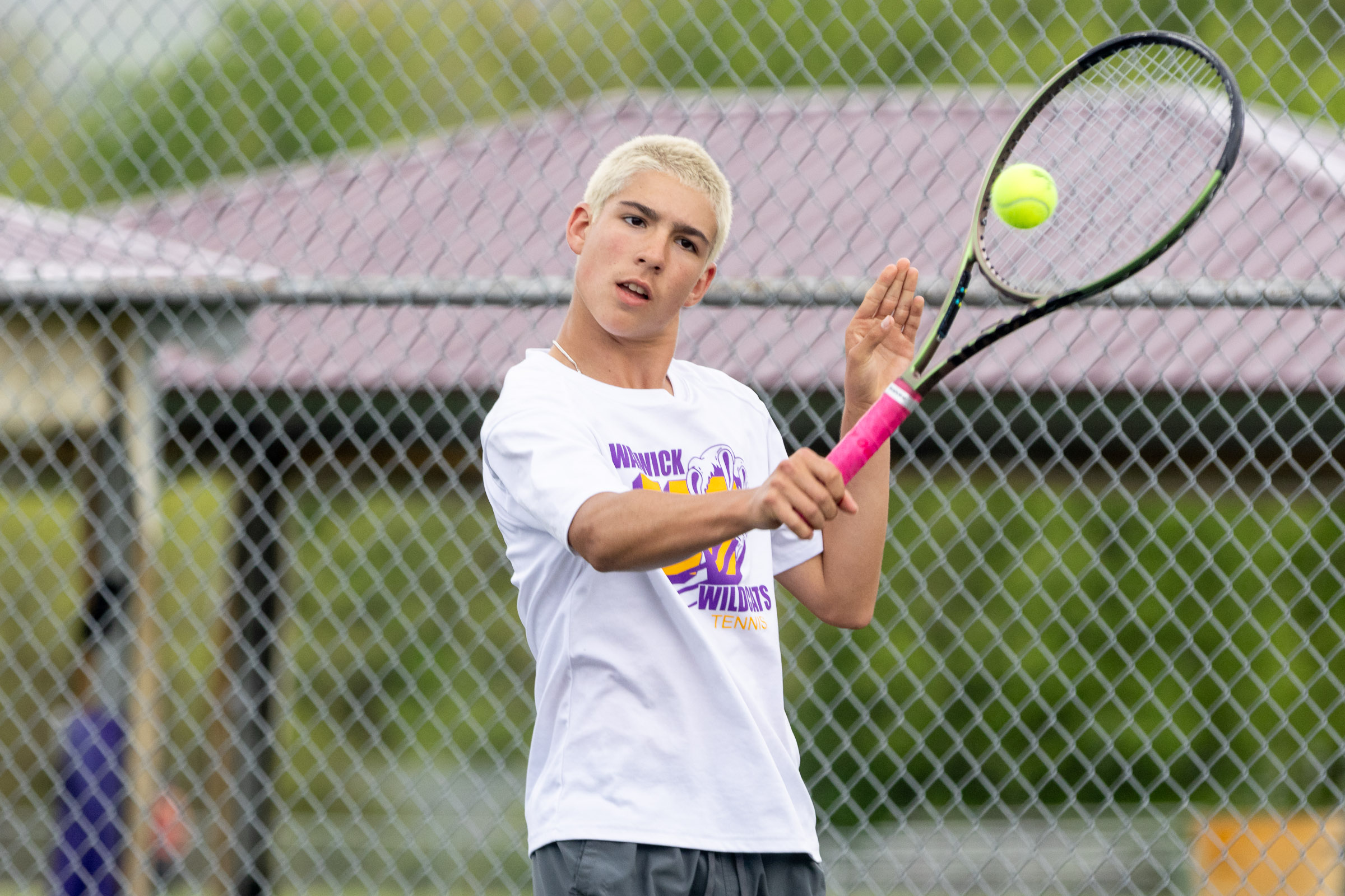 A Warwick Valley High School varsity boys tennis player hits the ball.