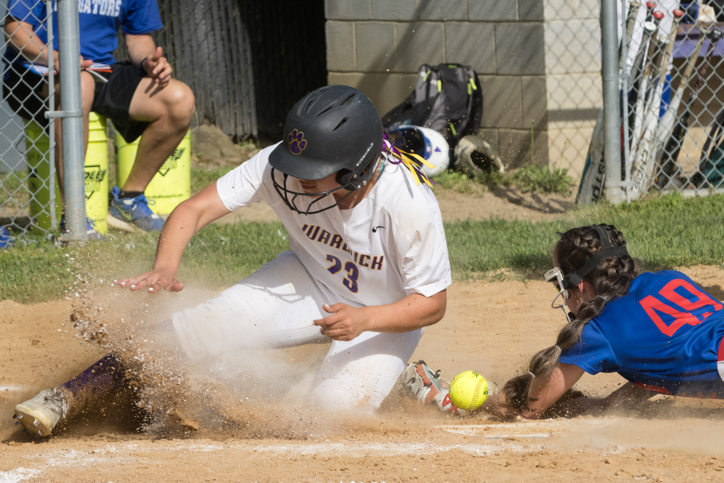 A Warwick Valley High School varsity softball player slides across home plate as the ball bounces away from the Goshen catcher.