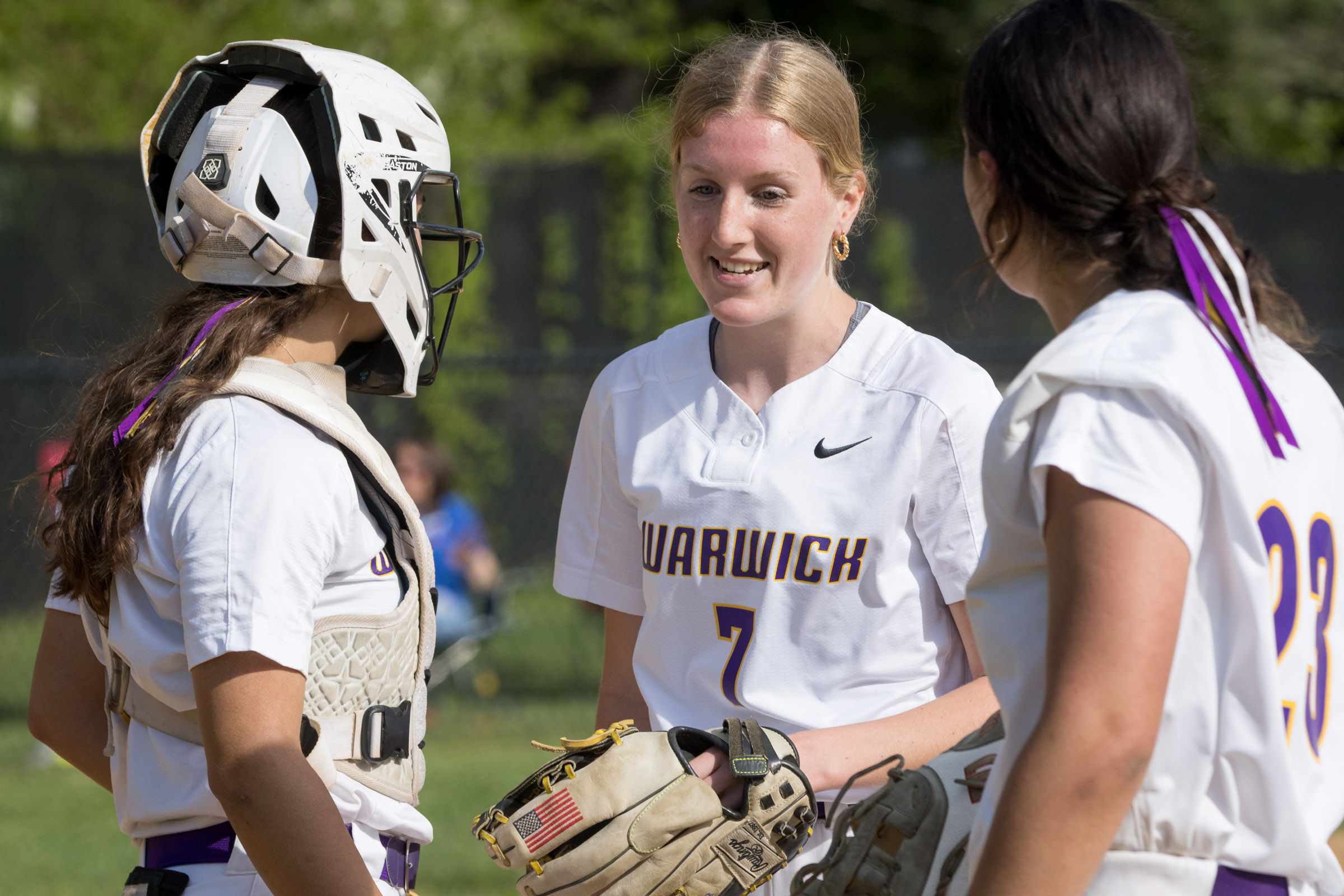 A Warwick Valley High School varsity softball pitcher smiles while talking to two teammates.