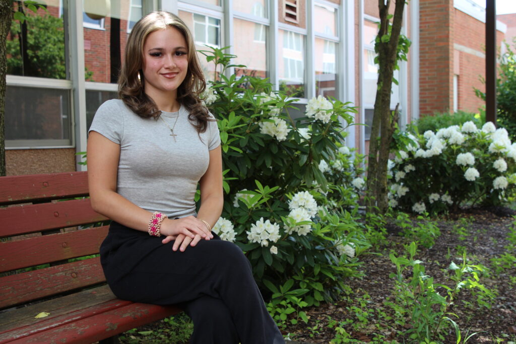 Ariana Elias sitting on a bench in front of flowers in the HS courtyard.