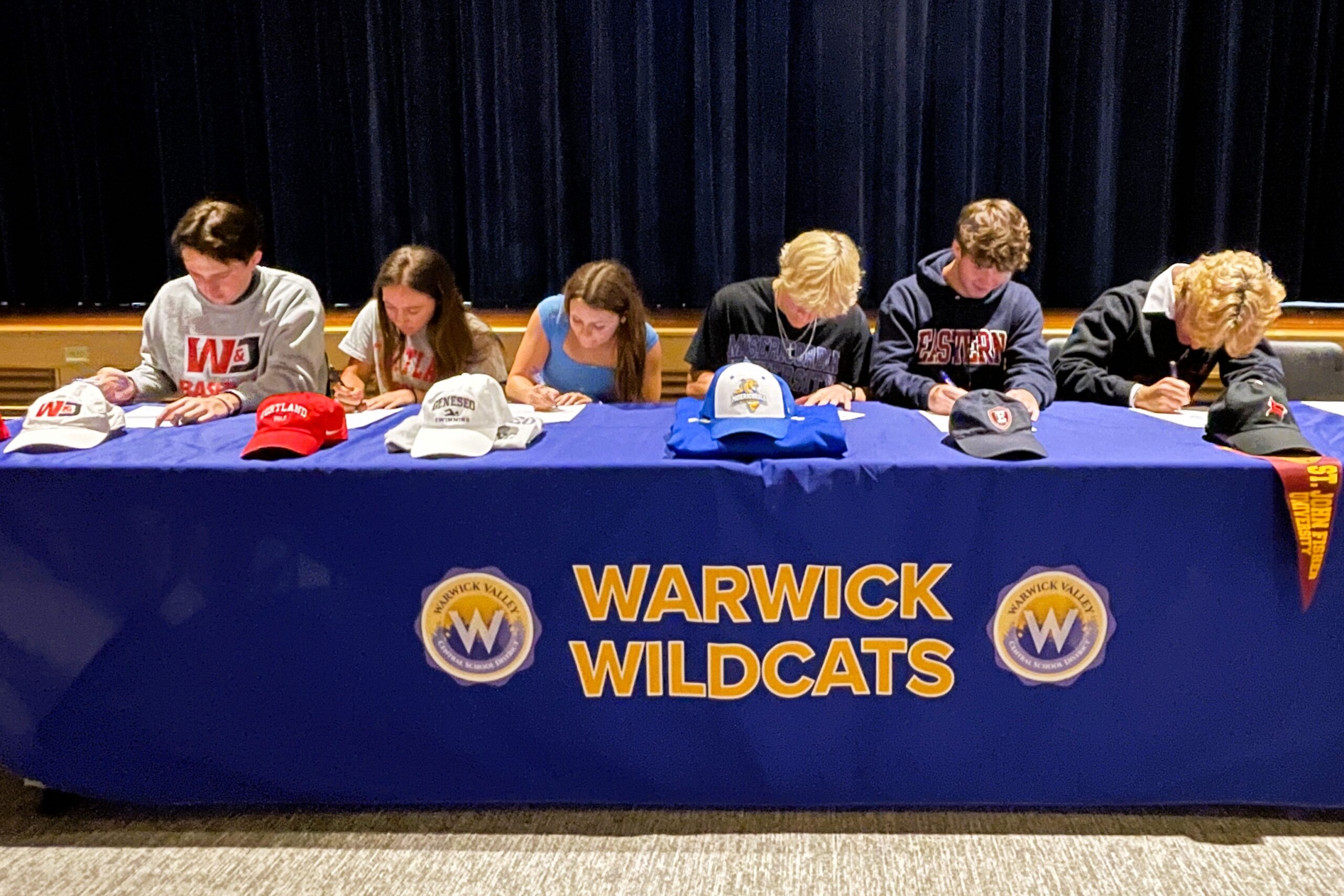 Warwick Valley High School athletes sit at a table to sign national letters of intent to play sports in college.