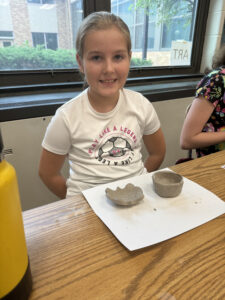 student smiling while sitting behind pottery creations