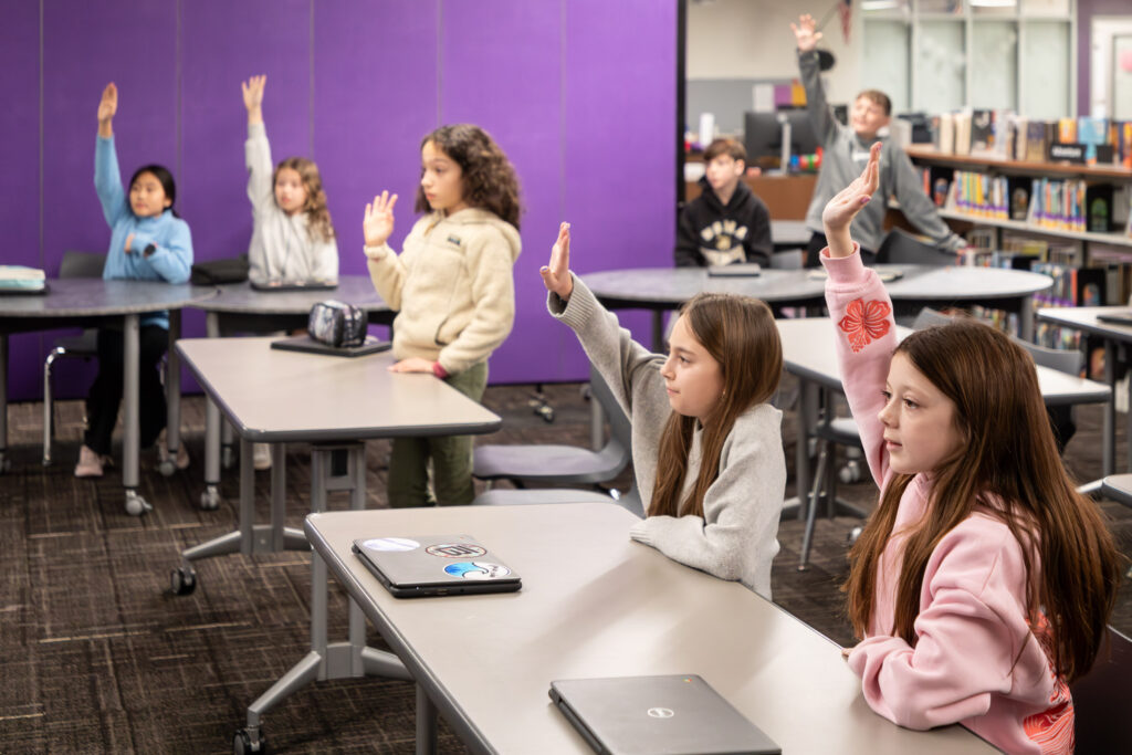 Warwick Valley Middle School students raise their hands in class.